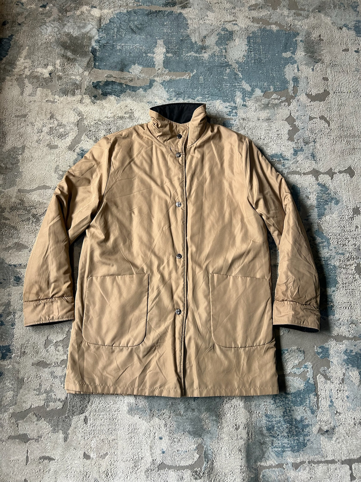 A tan waterproof jacket with a stand-up collar and front snap closure